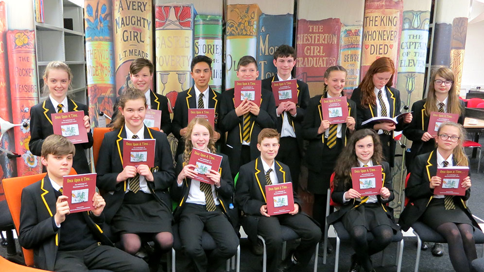 Seated school children holding up a books in the Library